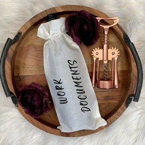 May include: A white fabric wine bottle bag with the text "Work Documents" printed on it. The bag is on a wooden tray with a rose and a rose gold corkscrew.