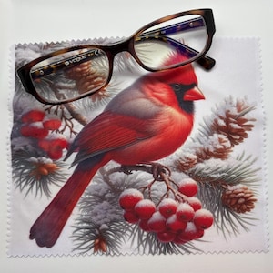 May include: Brown and tortoise shell eyeglasses rest on a microfiber cloth featuring a vibrant red cardinal bird perched on a snowy branch with red berries and pine cones. The glasses have a Vogue logo.