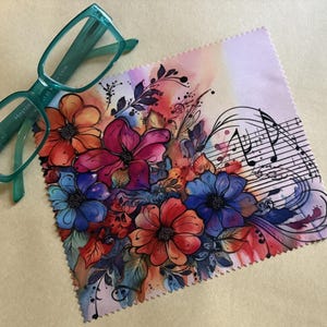 May include: A microfiber cleaning cloth with a watercolor design of flowers and musical notes. The cloth is white with a pink, orange, red, blue, and green floral design. The musical notes are black and white.