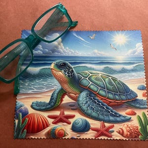 May include: A green microfiber cleaning cloth with a colorful illustration of a sea turtle on a beach with blue water and a bright sun. The turtle is green, blue, and brown with a detailed shell. The cloth has a scalloped edge.