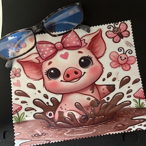 May include: A microfiber cleaning cloth featuring a cartoon pig in a mud puddle, wearing a pink bow. Pink butterflies and hearts decorate the cloth. A pair of eyeglasses with a black and gray frame rests on top.