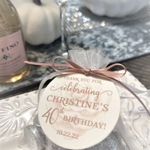 May include: A white favor bag with a pink and white round tag that says "Thank you for celebrating Christine's 40th Birthday! 10.22.22". The bag is filled with silver chocolate coins.