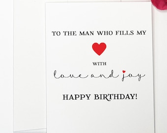 May include: A white card with black text that reads "To the man who fills my heart with love and joy. Happy Birthday!" There is a red heart in the centre of the card.