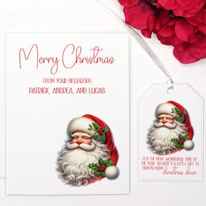 May include: A white Christmas card with red text that reads "Merry Christmas" and "From your neighbors Patrick, Andrea, and Lucas". A cartoon image of Santa Claus is in the bottom right corner. A white gift tag with red text that reads "It's the most wonderful time of the year so here's a little gift to spread some Christmas cheer" is attached to the card with a white ribbon.