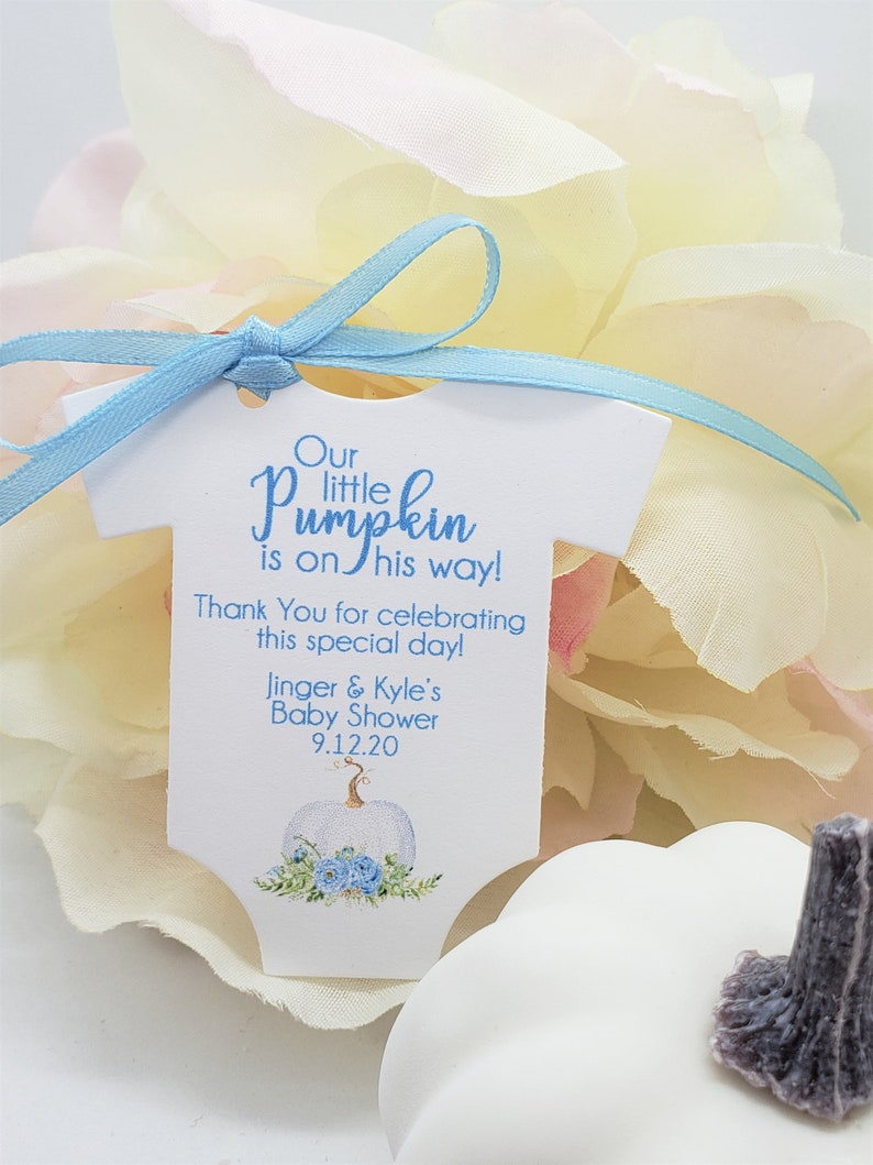 May include: A white baby onesie shaped tag with blue ribbon. The tag says "Our little pumpkin is on his way! Thank You for celebrating this special day! Jinger & Kyle's Baby Shower 9.12.20". The tag has a watercolor illustration of a white pumpkin with blue flowers.
