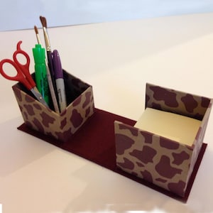 May include: A brown and tan desk organizer with a cheetah print design. The organizer has two compartments, one for pens and scissors and the other for sticky notes.