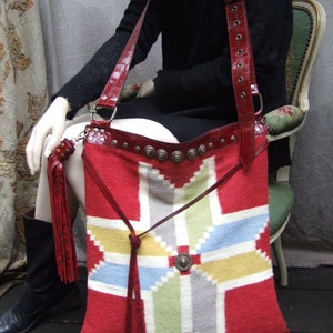 May include: A red, white, and blue woven tapestry bag with leather straps and metal accents. The bag has a geometric pattern and is worn over the shoulder.