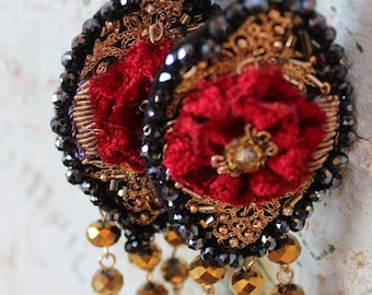 May include: A pair of dangle earrings with a red velvet flower design, black beads, and gold accents. The earrings have a long, dangling chain of gold beads.