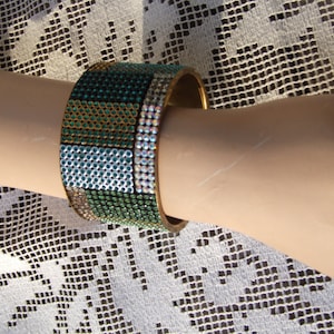 May include: A gold-toned bangle bracelet with a geometric pattern of green, blue, and gold rhinestones.