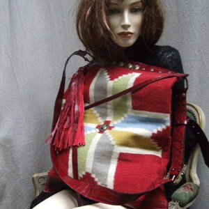 May include: A red, white, and blue patterned crossbody bag with a long fringe tassel. The bag is made of leather and has a geometric design.