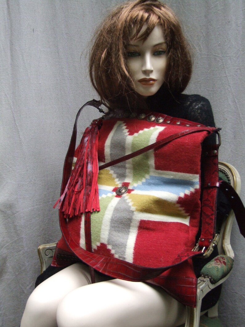 May include: A red, white, and blue patterned crossbody bag with a long fringe tassel. The bag is made of leather and has a geometric design.