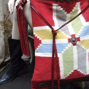 May include: A red, white, and blue patterned leather bag with a long fringe. The bag has a leather strap and metal accents.