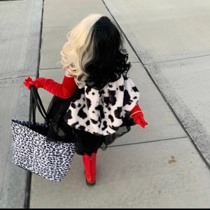 Pu&ograve; includere: Un bambino vestito da Cruella de Vil per Halloween. Indossa un cappotto con stampa dalmata bianco e nero, un vestito rosso, collant neri e stivali rossi. Porta una borsa tote con stampa dalmata bianco e nero.