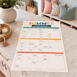 Peut inclure: Un grand calendrier mural en papier intitul&eacute; Summer Calendar avec des sections pour juin, juillet et ao&ucirc;t. Le calendrier pr&eacute;sente une grille avec des cases quotidiennes, des sections de notes et des en-t&ecirc;tes color&eacute;s en bleu sarcelle, orange et rouge.