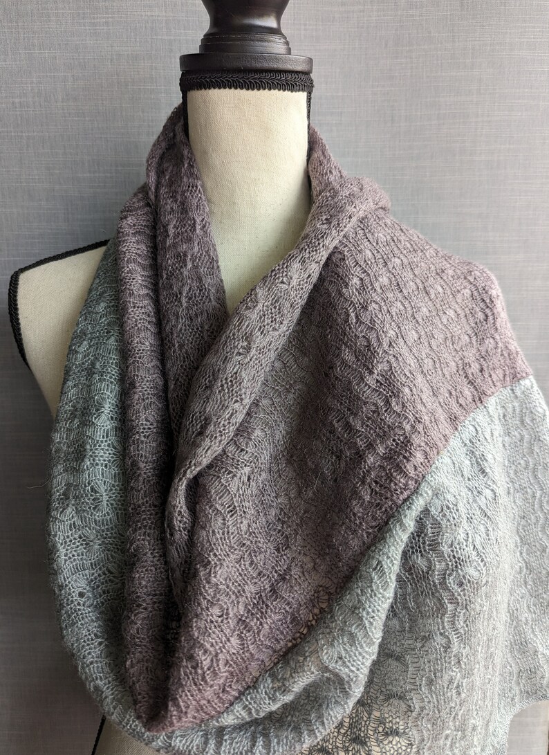 K&ouml;nnte beinhalten: Ein weicher, gestrickter Schal in Graut&ouml;nen und Blau. Der Schal ist &uuml;ber die Schultern einer Schaufensterpuppe gelegt und aus einem zarten, offen gewebten Stoff gefertigt.