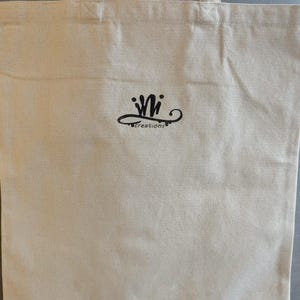 Może przedstawiać: Beżowa pł&oacute;cienna torba typu tote z uchwytem. Torba posiada czarne logo z napisem "Wi creations" w stylizowanej czcionce. Torba wykonana jest z wytrzymałej tkaniny w naturalnym kolorze, odpowiedniej do przenoszenia r&oacute;żnych przedmiot&oacute;w.