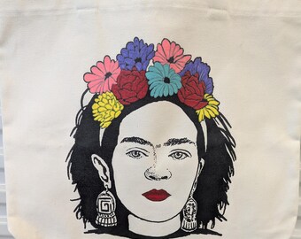 Op de afbeelding: Crèmekleurige draagtas met een zwart-wit portret van een vrouw met een bloemenkroon en rode lippenstift. De tas heeft crèmekleurige handvatten.