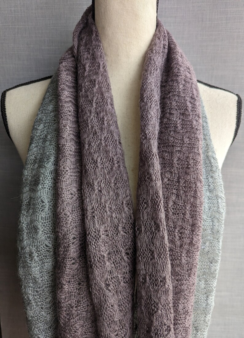 K&ouml;nnte beinhalten: Ein weicher, gestrickter Schal in zwei Graut&ouml;nen. Der Schal ist in der H&auml;lfte gefaltet und &uuml;ber den Hals einer Schaufensterpuppe gelegt. Der Schal ist aus einem leichten, atmungsaktiven Stoff gefertigt, der sich perfekt zum Schichten eignet.