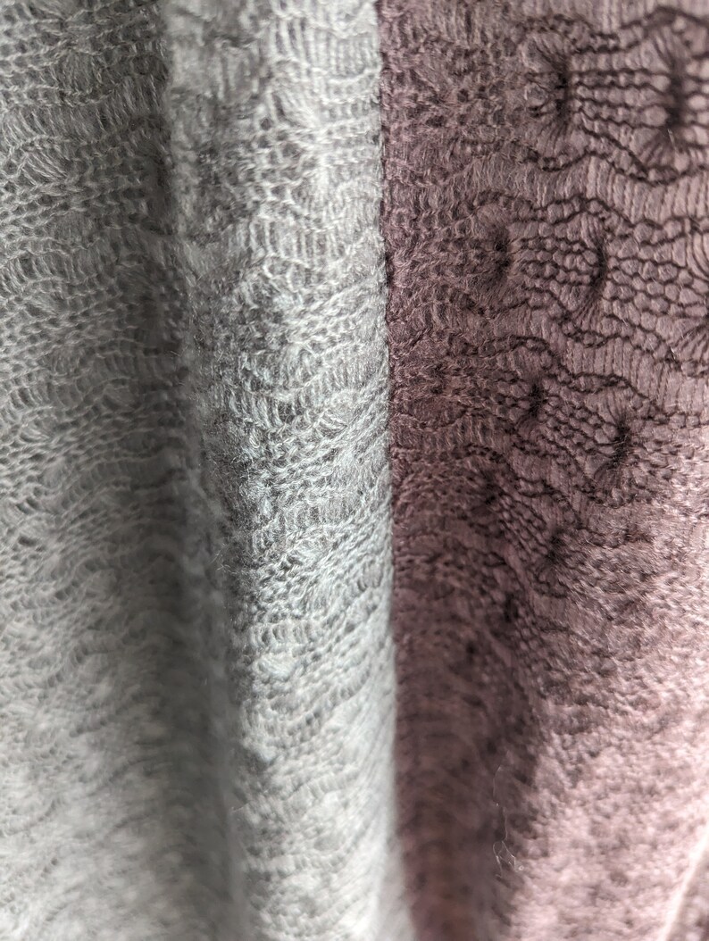 K&ouml;nnte beinhalten: Nahaufnahme eines weichen, gestrickten Stoffes mit einem zarten Spitzenmuster. Der Stoff ist links hellgrau und rechts dunkelgrau.