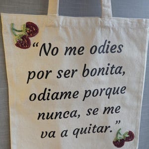 Może przedstawiać: Kremowa torba typu tote z czarnym tekstem: "No me odies por ser bonita, odiame porque nunca, se me va a quitar." Ozdobiona wzorami wiśni z koralik&oacute;w. Posiada dwa uchwyty do przenoszenia.