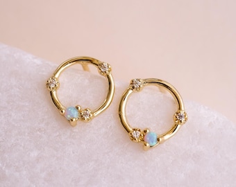 May include: A pair of gold hoop earrings featuring a small opal gemstone and tiny clear cubic zirconia stones set in the metal.