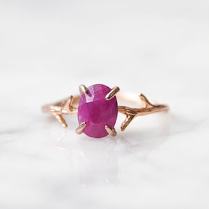 May include: A delicate gold ring with a branch design featuring a vibrant pink oval gemstone.
