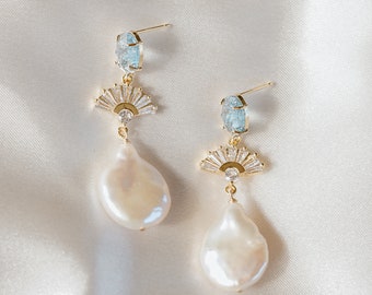 May include: A pair of gold-tone drop earrings featuring a light blue oval stone at the top, a fan-shaped accent set with clear baguette crystals in the center, and a dangling irregular white baroque pearl at the bottom of each earring.