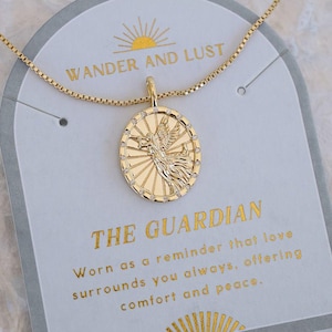 Puede incluir: Collar con colgante dorado con un dije ovalado con un dise&ntilde;o de p&aacute;jaro. El dije cuelga de una cadena delicada. El collar descansa sobre una tarjeta con el texto "WANDER AND LUST" y "THE GUARDIAN".