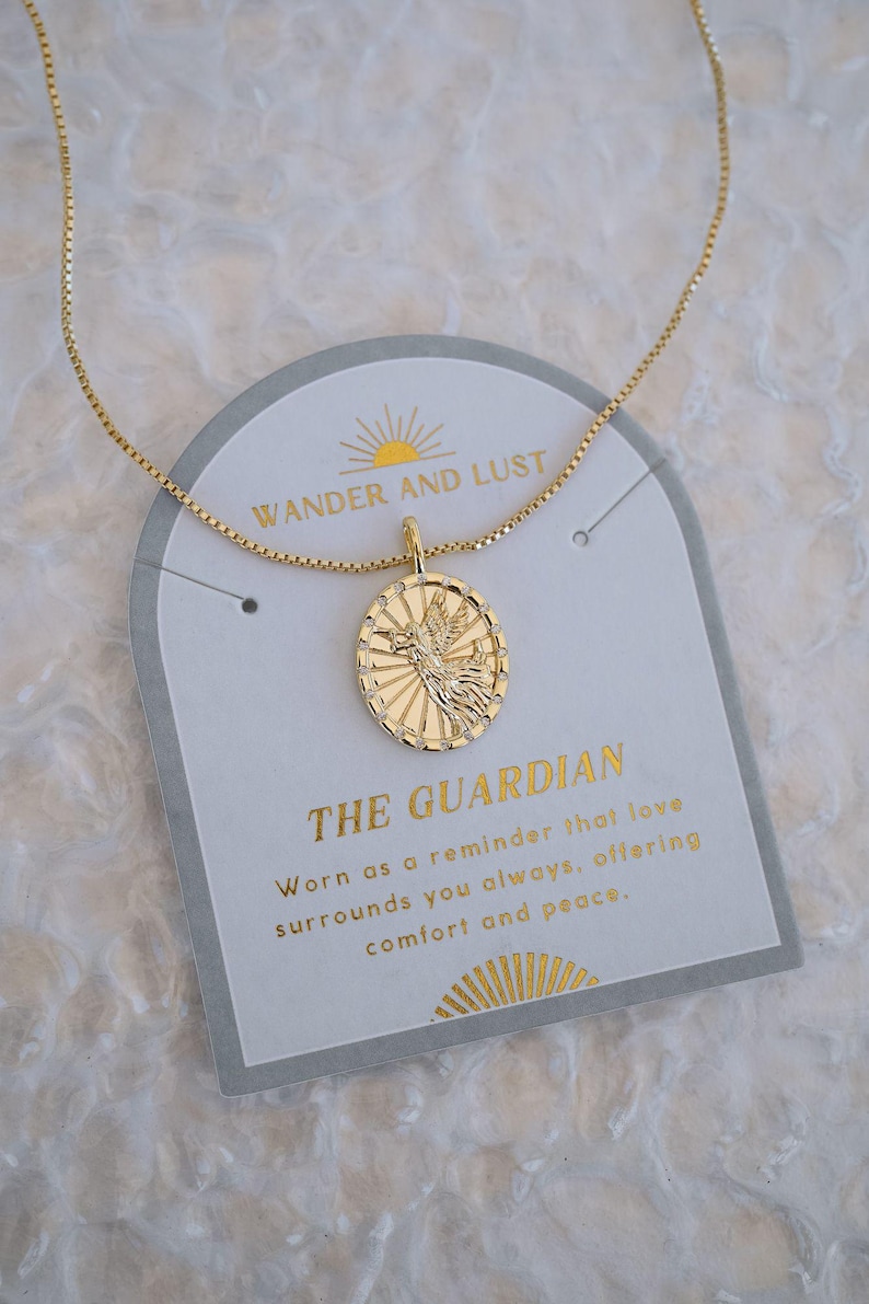 Puede incluir: Collar dorado con un colgante con un dise&ntilde;o de p&aacute;jaro dentro de un marco ovalado. El collar se muestra en una tarjeta que dice "WANDER AND LUST" y "THE GUARDIAN". La tarjeta tambi&eacute;n incluye texto sobre el amor, el consuelo y la paz.
