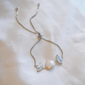 May include: A silver adjustable bracelet with a pearl and two crystal accents. The bracelet is made of a delicate chain and has a sliding clasp.
