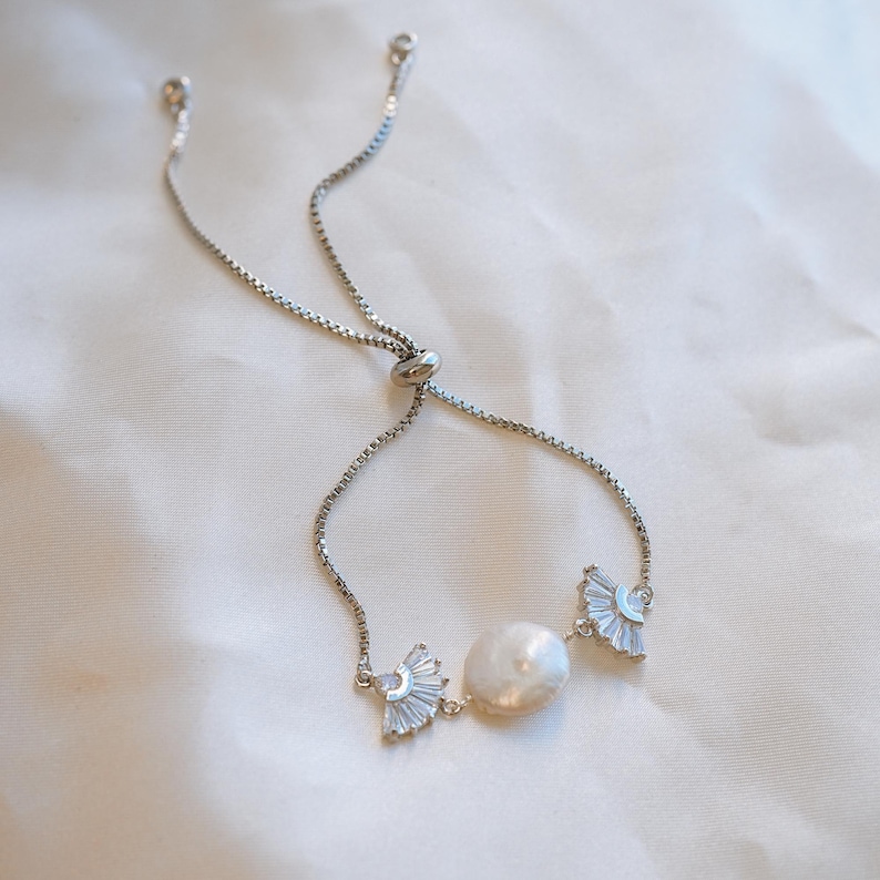 May include: A silver adjustable bracelet with a pearl and two crystal accents. The bracelet is made of a delicate chain and has a sliding clasp.
