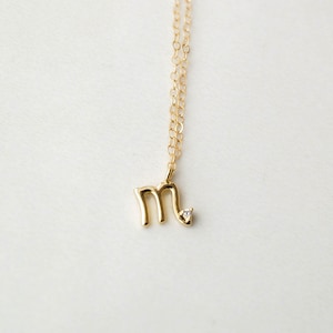 May include: A gold chain necklace with a small gold pendant in the shape of the letter "M" with a single diamond accent.
