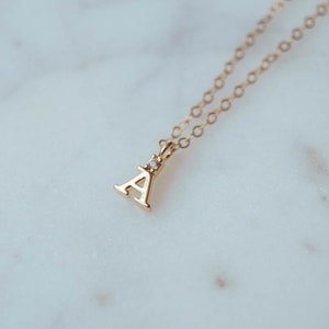 May include: A gold chain necklace with a small gold letter A pendant featuring a single clear stone accent.