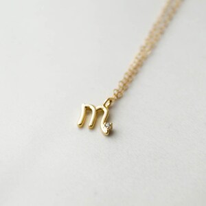 May include: A gold necklace with a small letter 'M' pendant and a single diamond accent.