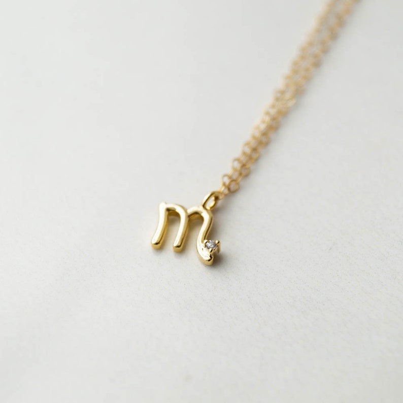 May include: A gold necklace with a small letter 'M' pendant and a single diamond accent.