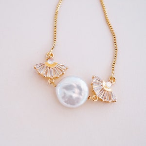 May include: A delicate gold chain necklace with a large white pearl and two gold fan-shaped charms adorned with clear rhinestones.
