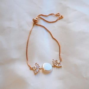 May include: A delicate gold chain bracelet with a pearl and two crystal accents. The bracelet is adjustable with a sliding clasp.