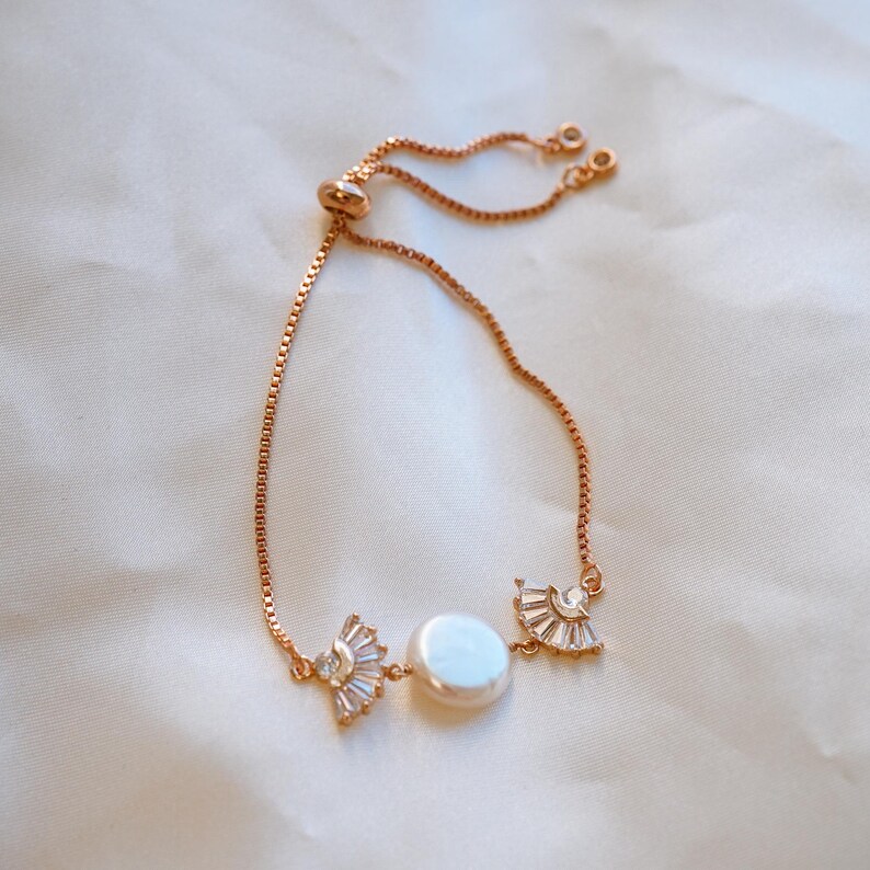 May include: A delicate gold chain bracelet with a pearl and two crystal accents. The bracelet is adjustable with a sliding clasp.