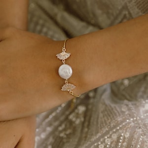 May include: A gold bracelet with a large white pearl and two gold fan-shaped charms.