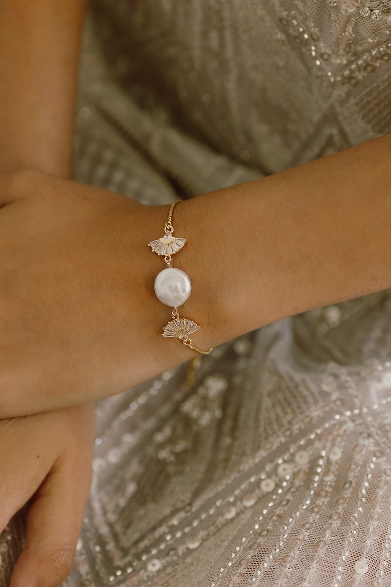 May include: A gold bracelet with a large white pearl and two gold fan-shaped charms.