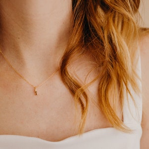 May include: A close-up of a woman wearing a white top with a delicate gold necklace featuring a small diamond pendant.