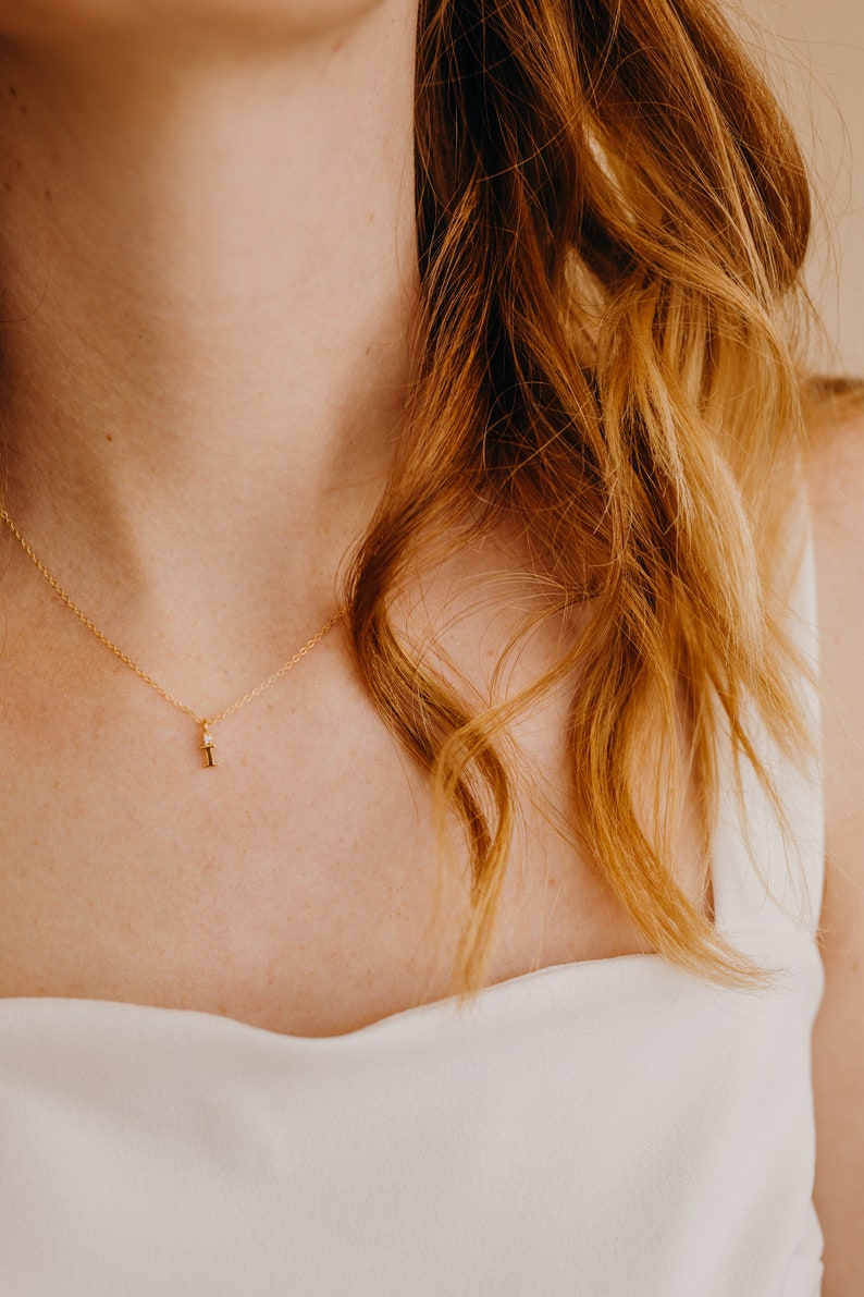 May include: A close-up of a woman wearing a white top with a delicate gold necklace featuring a small diamond pendant.