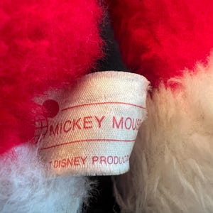 May include: Close-up of a plush toy with red and white fur. A tag with the words "MICKEY MOUSE" and "DISNEY PRODUCTS" is visible. The toy's fur appears soft and fluffy.
