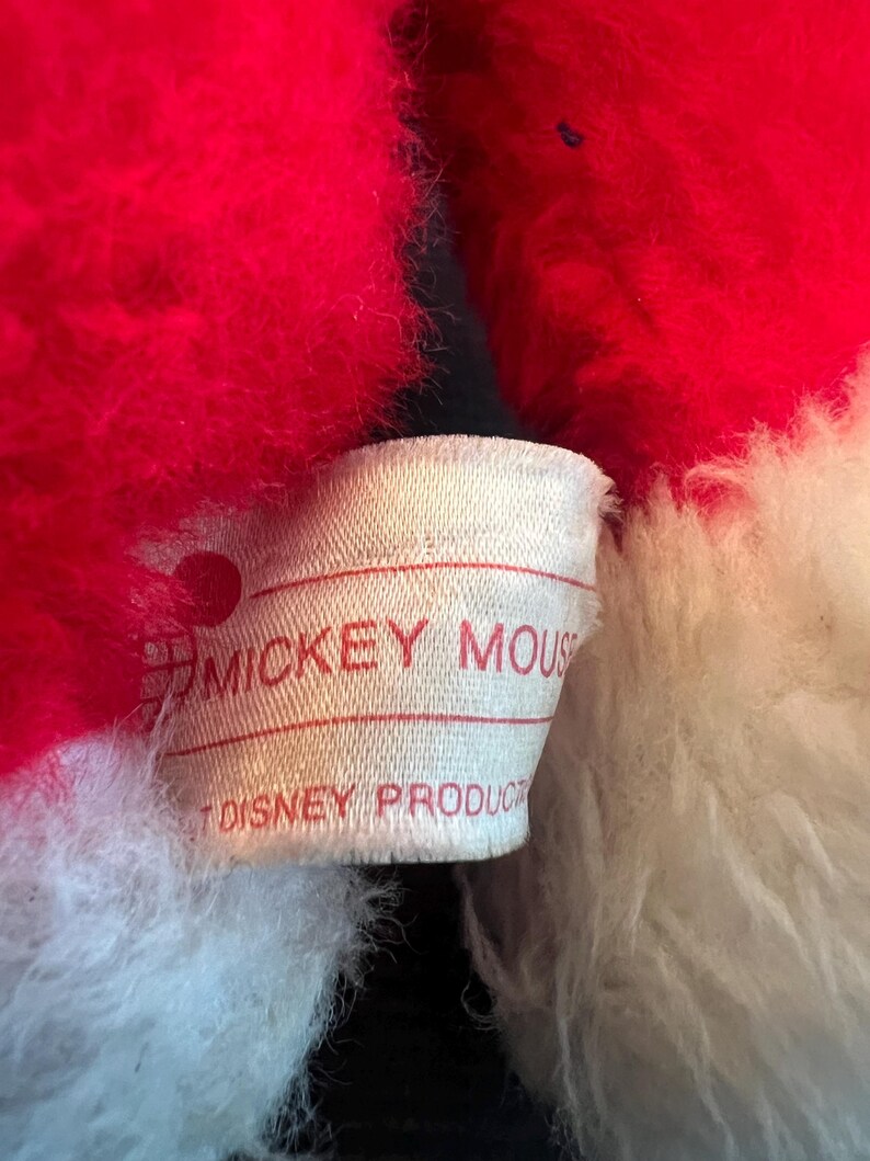 May include: Close-up of a plush toy with red and white fur. A tag with the words "MICKEY MOUSE" and "DISNEY PRODUCTS" is visible. The toy's fur appears soft and fluffy.