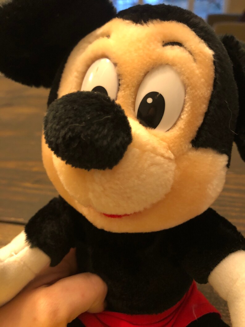 Puede incluir: Un juguete de peluche Mickey Mouse negro y blanco con una pajarita roja y blanca. El juguete tiene una gran sonrisa y ojos grandes.