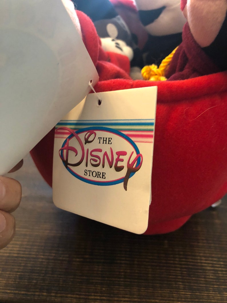 Peut inclure: Une tasse &agrave; th&eacute; en peluche rouge avec une poign&eacute;e en corde jaune. La tasse est remplie de personnages en peluche, dont Mickey Mouse, Minnie Mouse et Dingo. La tasse a une &eacute;tiquette blanche attach&eacute;e &agrave; elle qui indique "The Disney Store".