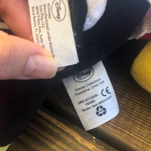May include: White and black plush toy with a white tag that reads "Disney Collection Pasadena, CA91105 FAC-011309-15255 Vendor Item #KD121221 CE".