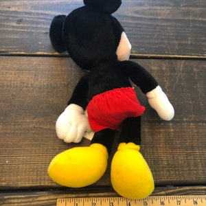 May include: A black and red plush Mickey Mouse toy with yellow shoes. The toy is approximately 15 inches tall and is sitting on a wooden surface.