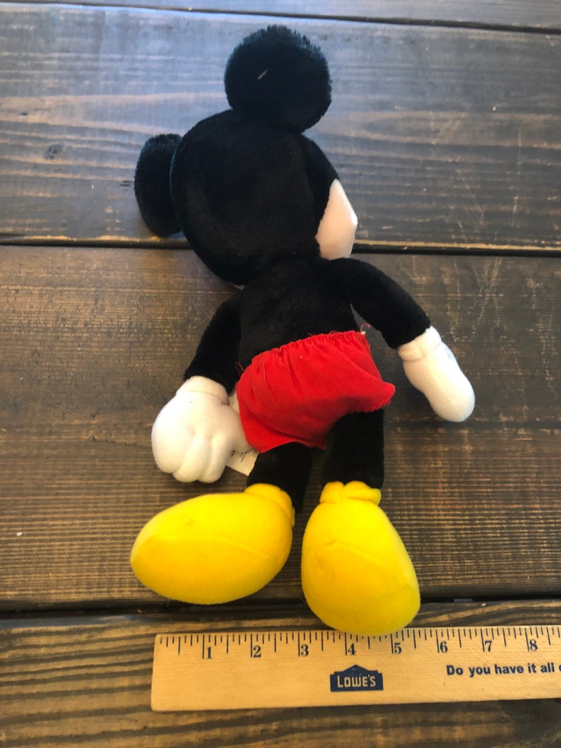 May include: A black and red plush Mickey Mouse toy with yellow shoes. The toy is approximately 15 inches tall and is sitting on a wooden surface.
