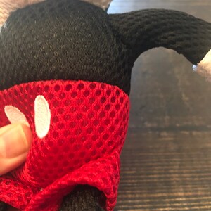 May include: Red, black, and white plush toy shaped like Mickey Mouse. The toy is made of a mesh material and has a red, white, and black design.